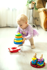 girl plays logical pyramid on floor in living room on sunny day. Montessori wooden toy folded pyramid. Circle, quadra, triangle, rectangle wooden elements of children's toys. Soft focus