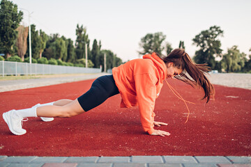 Young woman doing warm-up exercises on sportsground early in the morning