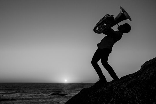 Silhouette of a musician with a trumpet on the seashore. Black and white photo.