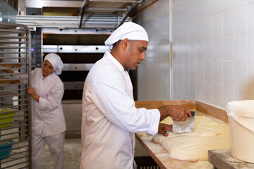 Portrait of confident latin american bakery owner engaged in breadmaking, preparing portioned pieces of dough for baking