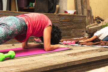 young woman training yoga on pink mat in wood terrace red t-shirt