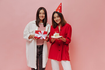 Joyful happy girls in good mood pose on pink background and celebrate birthday. Woman in red blouse...