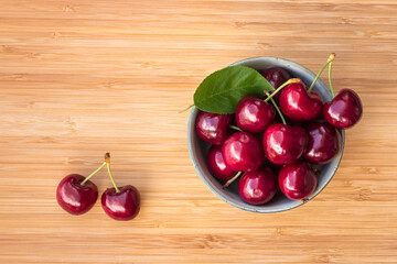 closeup of ripe dark red stella cherries in porcelain bowl on wooden chopping board with copy space