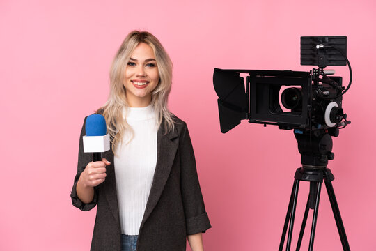 Reporter woman holding a microphone and reporting news over isolated pink background laughing