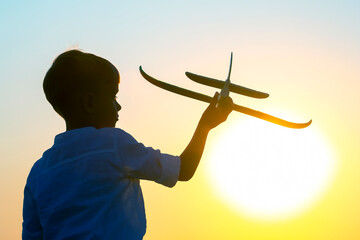 silhouette of a boy lets a model plane fly into the sky against the backdrop of the setting sun. Children's dream of a future pilot