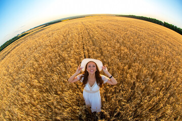 Happy woman stands in a wheat field in the summer against the background of a setting sun