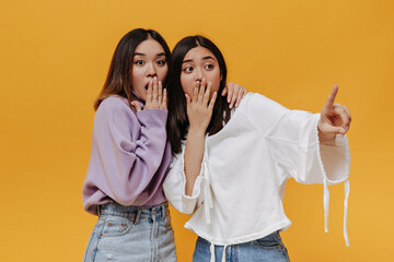 Portrait of shocked Asian brunette women on isolated. Young surprised girls in hoodies cover...