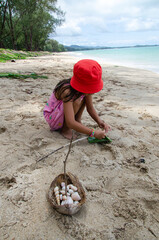 Obraz premium Little girl with a red hat plating sand alone on the sea beach. She use her imagination creating a big ship carring her sea shell collection.