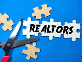 Business concept.Text REALTORS writing on jigsaw puzzle with scissors on blue background.