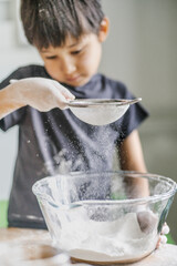 The child cooks in the kitchen. Sifts the flour.