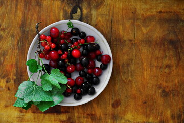 Set of mixed assorted fresh juicy ripe berries red and black currants, cherries in plate on wooden table. Top view