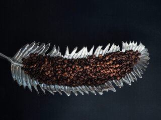 Coffee beans in tray, silver color palm leaf shape isolated on dark background, top view.