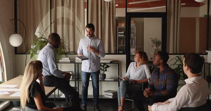 Educational corporate training event concept. Millennial skilled coach provide helpful information share knowledge to diverse company members, staff listen to mentor at briefing meeting in office room