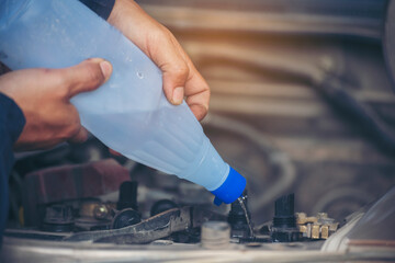 Car Mechanic man hands pouring Deionized purified Distilled water for car battery mechanical service. Close up hands man hold Deionized Distilled liquid water bottle at garage auto mobile car service