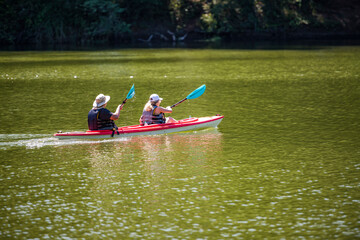 Two elderly women rowing oars synchronously while kayaking on the lake