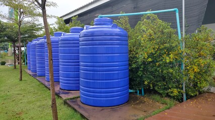 Rows of blue water tanks. Plastic buckets back up water on the cement floor behind a public restroom with copy space.