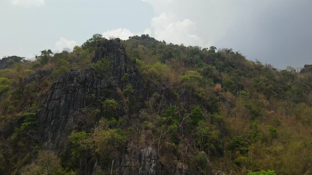 4K aerial tracking shot of beautiful limestone rocky cliff covered with lush green forest found in the mountain range in Thailand Southeast Asia.