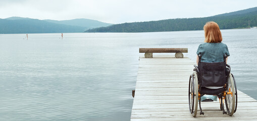 Woman in wheelchair watching girls surf. Panoramic image with copy space