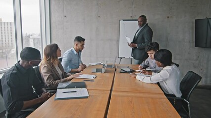 Mature african american businessman mentor leader boss holding papers enters in boardroom to meeting with diverse multiracial business management team group talking about new strategy plan project
