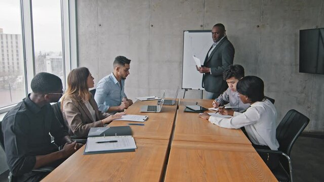 Mature african american businessman mentor leader boss holding papers enters in boardroom to meeting with diverse multiracial business management team group talking about new strategy plan project