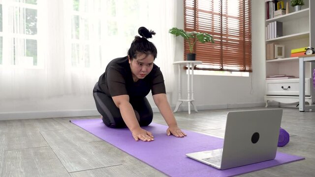 Fat or Big woman in black workout clothes is using a wireless laptop to watch yoga, exercise, stay healthy.