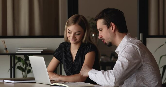 Attractive female mentor making corporate software review for new comer employee, help with program provide explanations guidance to apprentice seated together at desk use laptop. Coaching concept