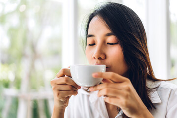 Portrait of smiling happy cheerful beautiful pretty asian woman relaxing drinking and looking at cup of hot coffee or tea.Girl felling enjoy having breakfast in holiday morning vacation on bed at home