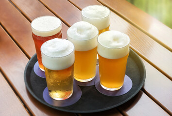 Five cold beers with frothy heads in glasses on a tray