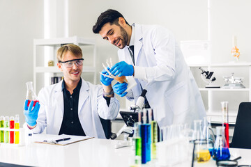 Professional two scientist man research and working doing a chemical experiment while making analyzing and mixing liquid in test tube.Young science man dropping sample chemical on glass at laboratory