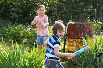Cheerful girl and boy shooting water pistols in the backyard