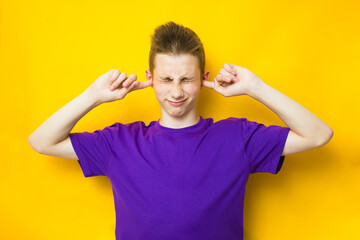 Fototapeta na wymiar Emotional teen boy covering ears with fingers on yellow background