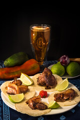 Appetizer made with tortilla and delicious fried pork rinds on a plate decorated with a tridicional tablecloth with lemons and chili with onion on a black background