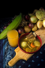 overhead view of a traditional Latin American dish of beef soup with vegetables and spices next to a glass of natural passion fruit soft drink on a traditional Costa Rican tablecloth