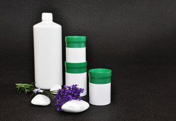 Fototapeta na wymiar white plastic bottle and jars for spa products decorated with white stones and lavender and free space for text on black background