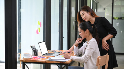 Two female colleagues using smart phone together during break in office.