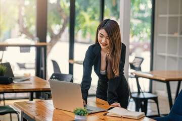Asian businesswoman standing at the office with a laptop and a notebook at the office.