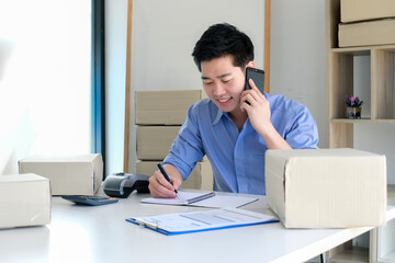 Small business owner Asian man sitting at home working and talking on the phone taking notes on...