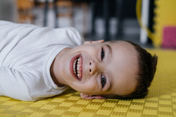 Happy child on the mat in child rehabilitation center. Boy with cerebral palsy smiling....