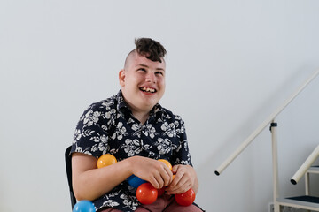 Happy teenage child over white wall in rehabilitation center. Boy with cerebral palsy smiling, playing with balls. Rehabilitation and inclusion kindergarten, day care. Disabled kid, positive emotions 