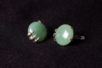 Women's earrings. A green stone in a metal frame. On a black background.