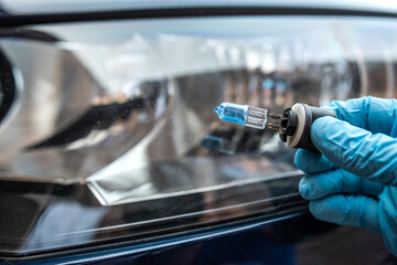 mechanic hold car halogen light bulb for repair against headlight auto in background