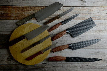 Top Views of Professional kitchen knife set arranged in rows with wooden chopping board isolated on wooden background. Warning, please use it carefully.