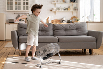 Little preschool boy enjoy fresh air flow from fan. Cute small kid play with ventilator blowing...