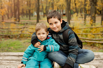 Fototapeta na wymiar Two brothers play outdoors in autumn, best friends. Two happy boys in the woods. Cute brothers who are smiling happily together.Little brother with brother sit at the outdoor. Fraternal relations