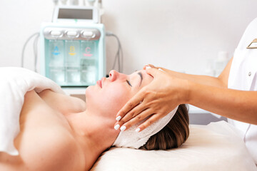 Cosmetologist massages the woman's face. Cosmetic equipment in the background. Portrait of the client and the doctor's hands in close-up. Side view. Concept of cosmetology and treatment