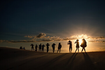 Fototapeta na wymiar Shadows on the sandy beach and Silhouette of people's group walking across the dunes in Vietnam during sunset