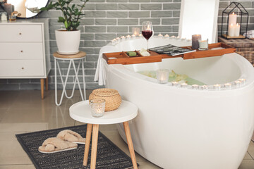 Stylish interior of modern bathroom with burning candles and glass of wine