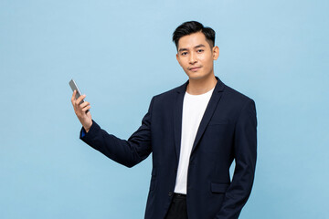Young handsome Asian man in semi formal suit holding mobile phone and looking at camera in light...