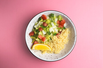 Bulgur with vegetables in a plate over pastel pink background. Delicious healthy dish in a bowl