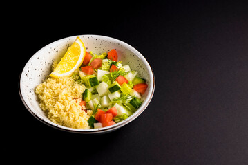 Bulgur with vegetables in a plate over black background. Delicious healthy dish in a bowl